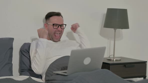 Casual Man Celebrating Success on Laptop in Bed