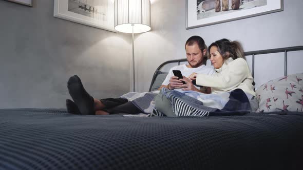Couple lying in bed with mobile phones in hands