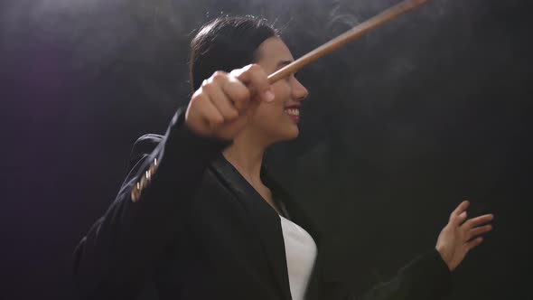 Side View Of Asian Conductor Woman Holding A Baton And Showing Gesture Quickly In The Black Studio