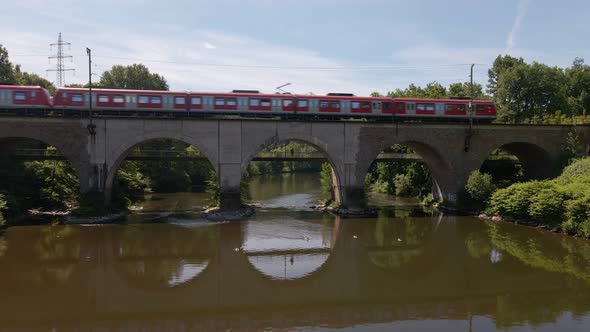 Red passenger train crossing a brick trestle in Germany on a sunny spring day. Static wide angle vie