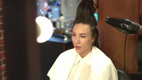 Reflection in Mirror of Confident Young Woman Sitting in Beauty Salon with Unrecognizable Tattooed