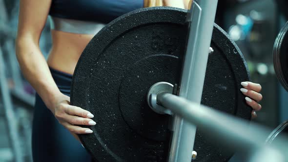 Strong woman putting weight plate on barbell in gym