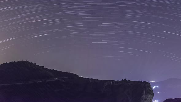 Time lapse of startrails moving on the nightsky over silhouette of rock and Monastery, Greece