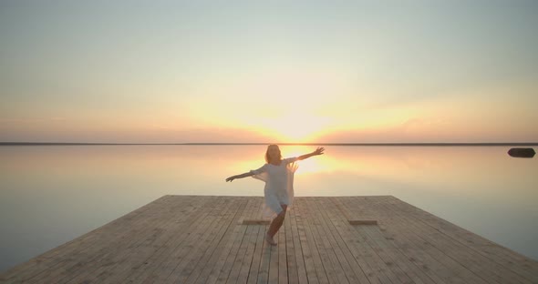 Young Woman Dancing on the Wooden Pier of the Lake Sunset View