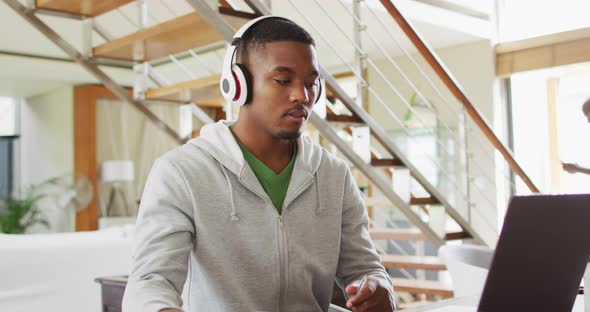 African american teenage son wearing headphones using a laptop with father in background