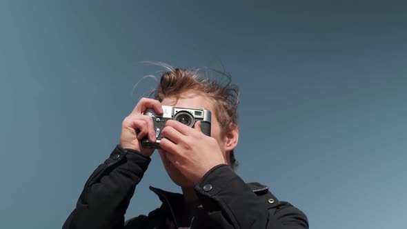 A Blond Man Takes a Closeup Photo with a Retro Camera on a Sunny Day