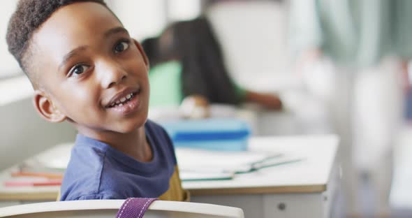 Video of happy african american boy sitting at desk during lesson in classroom alt