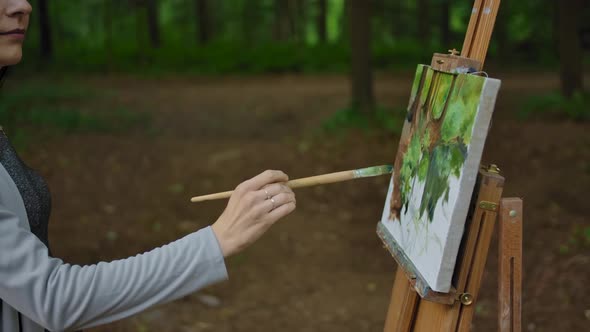 Side View of a Woman's Hand Painting a Landscape on Canvas in a Park