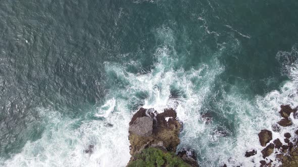 Top down aerial view of giant ocean waves crashing and foaming in coral beach