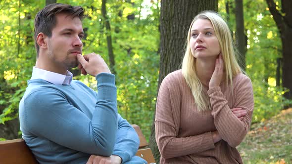 A Man and a Woman Sit on a Bench in a Park on a Sunny Day and Think About Something