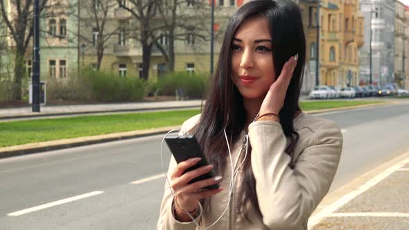 A Young Asian Woman Listens To Music on a Smartphone in a Street in an Urban Area