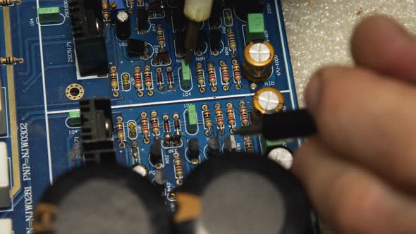 The repairman uses a tester to check the pins on the blue motherboard