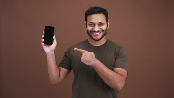 Cheerful Positive Indian Man Showing Cellphone with Blank Screen and Pointing at It Smiling to