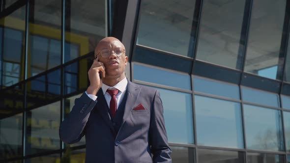 Young Attractive African American Businessman Talking on the Phone Near a Modern Mirror Building