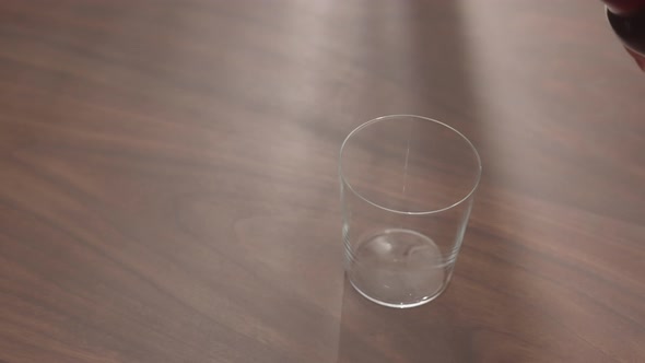 Slow Motion Pour Red Drink in Tumbler Glass on Walnut Table with Copy Space