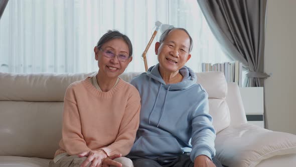 Portrait of Asian happy senior elder mature couple sit on sofa and smiling in living room at home.