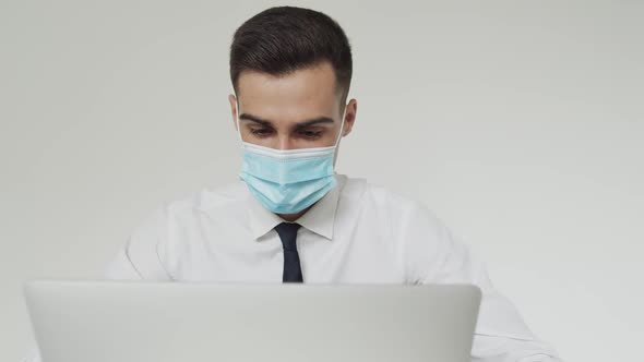 Portrait of Male Student with Medical Mask Thinks During a Studying on a Laptop
