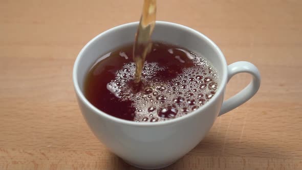 Pouring brewed black tea into a white cup close-up 