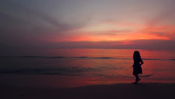 Silhouette of a Woman Walking at the Beach at Beautiful Dusk