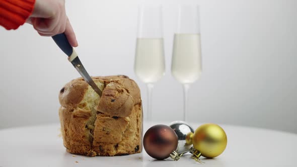 Cutting Traditional Christmas Panettone with Knife on Table with Champagne and New Year Balls
