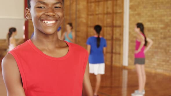 Smiling school boy holding a basketball while team playing in background