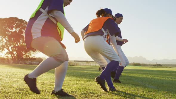 Diverse group of female baseball players exercising on pitch, running and touching the ground