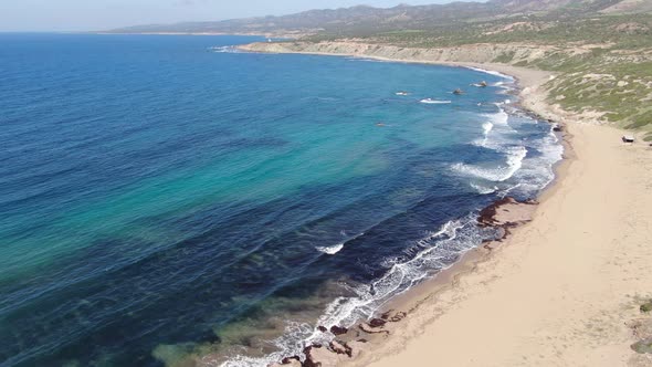 Aerial View of Blue Lagoon with Green Sandy Hills Around. Cold Waves Rolling on Beach and Crashing