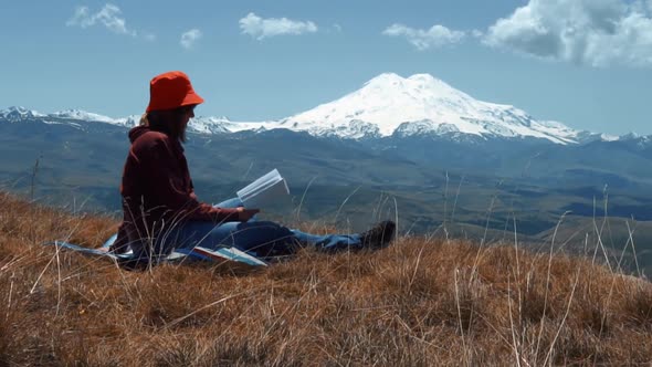 Girl Reads a Book on a Background of Mountains