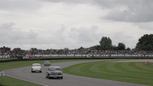 Track-side view of old cars racing side by side into turn one at the Goodwood Revival Car Festival.