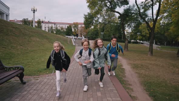 Front View of Caucasian Schoolkids with Schoolbags Running in the School Yard at School