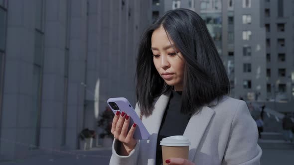 Pivoting Portrait of an Asian Woman Holding a Smartphone in a Business Centre and Looking Away