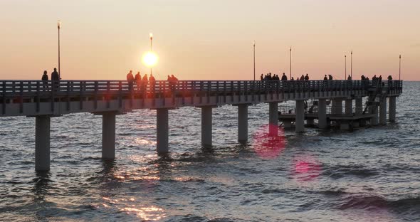 Silhouettes of People Walking on the Pier Against the Sunset. Local People Are Fishing, Tourists Are