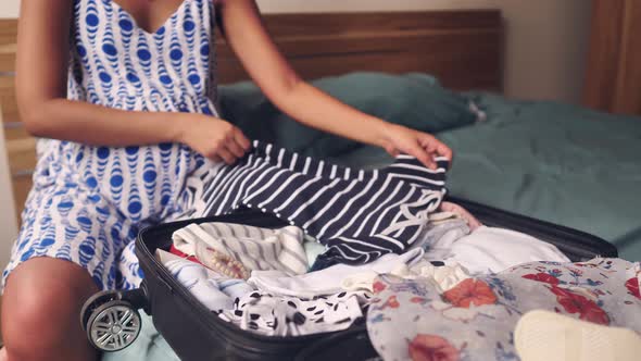 A Close Up View of a Pregnant Woman Sitting on the Bed Packing Clothes and Placing It Into the