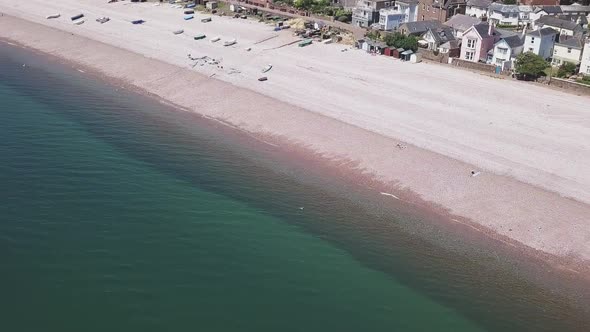Pan past colorful huts and boats on the Budleigh Salterton Jurassic Coastline beach, AERIAL STATIC C
