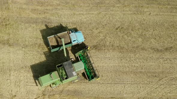 Combine harvester unloads grain to the dump truck.