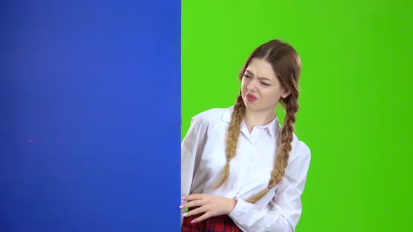 Girl Looks Out From Behind a Blue Board and Shows a Thumbs Down . Green Screen