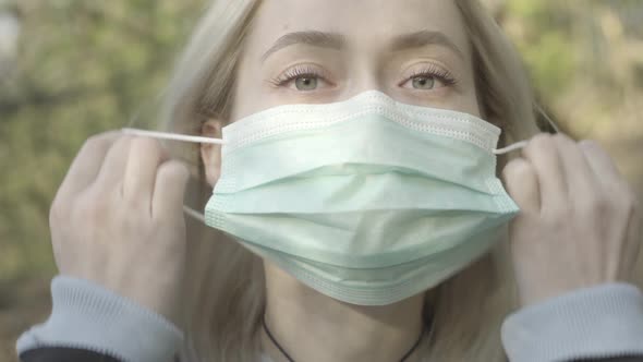 Extreme Close-up of Young Blond Woman Taking Off Face Mask and Smiling at Camera. Portrait of