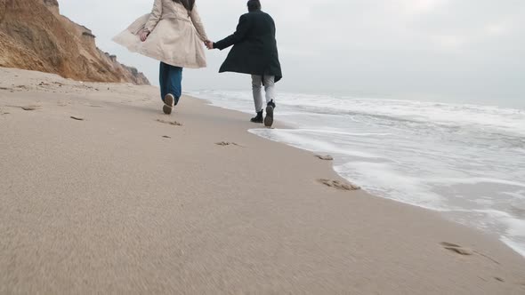 Happy Couple Walking on the Wild Beach on Cloudy Sunrise or Sunset