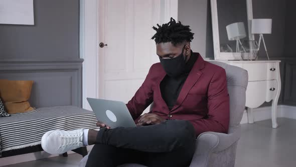 Black Business Man Works Behind a Laptop in a Protective Mask