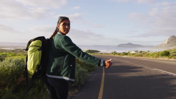 African american woman with backpack trying to hitch a lift while standing on the road