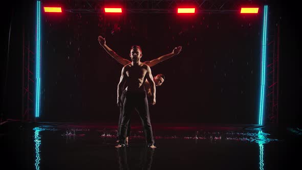 A Group of Muscular Men with a Naked Torso Perform Acrobatic Exercises. Shot in a Dark Studio with