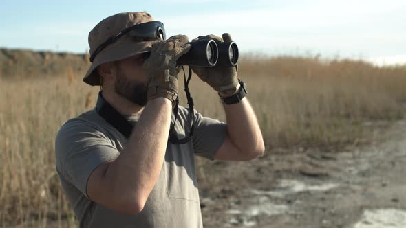 Side View of Bearded Adult Man Hunter of a Guard in Military Tshirt and Hat Looking Through