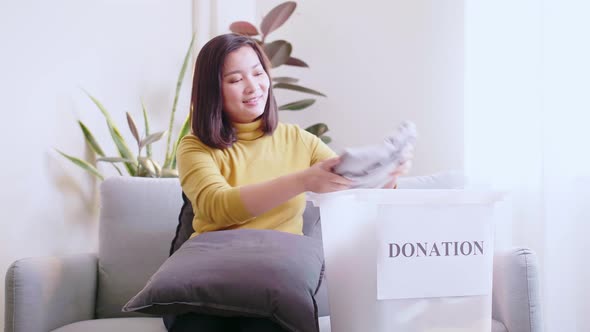 Young Asian woman selecting clothes for donation and making reservations for delivery and pay by cre
