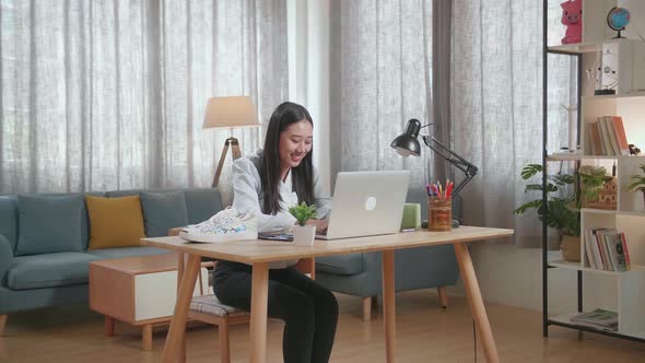 Smiling Asian Female Footwear Going Through The Room, Sits Down And Starts Working At Her Laptop