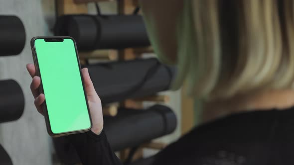 back view of fitness woman using green screen smart phone at home. Woman preparing for workout