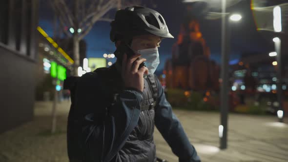 Cyclist in Helmet and Protective Mask Commuter with Bicycle on Way Home From Work Talking on Phone