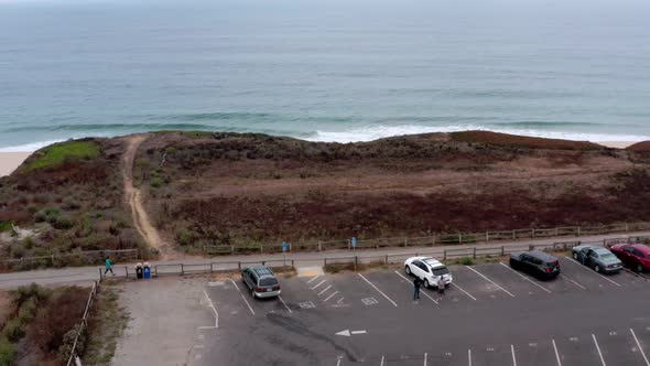 AERIAL: drone, half moon bay beach cliffs , parking lot and people, flying away view