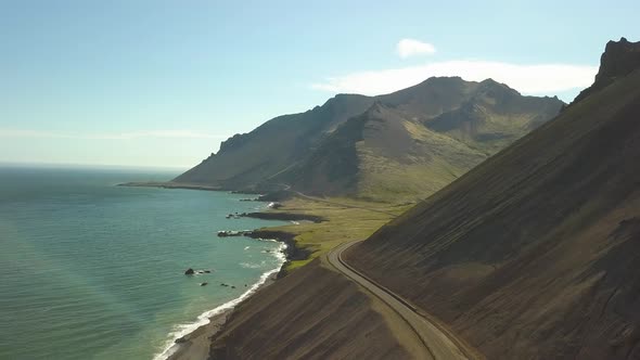 Aerial orbit of hillside road near turquoise sea, hills in background in in Djúpivogur small town ne