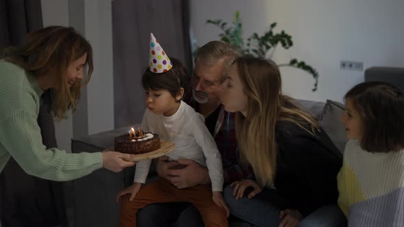 Little Boy Blows Out the Candles on Dream the Cake in a Circle of Happy Family