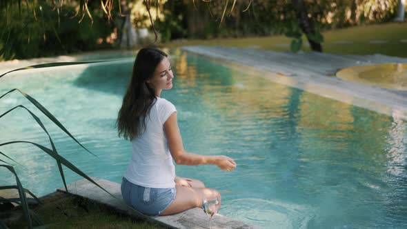 Girl in Tshirt and Denim Shorts Drinks Water Near Pool